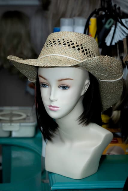 A styled wig on a mannequin head wearing a straw cowboy hat.